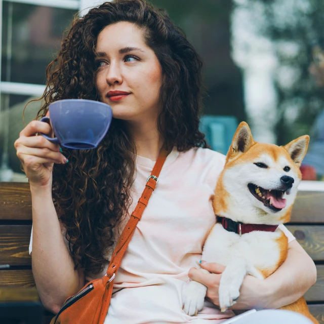 A woman drinking coffee while holding her happy dog